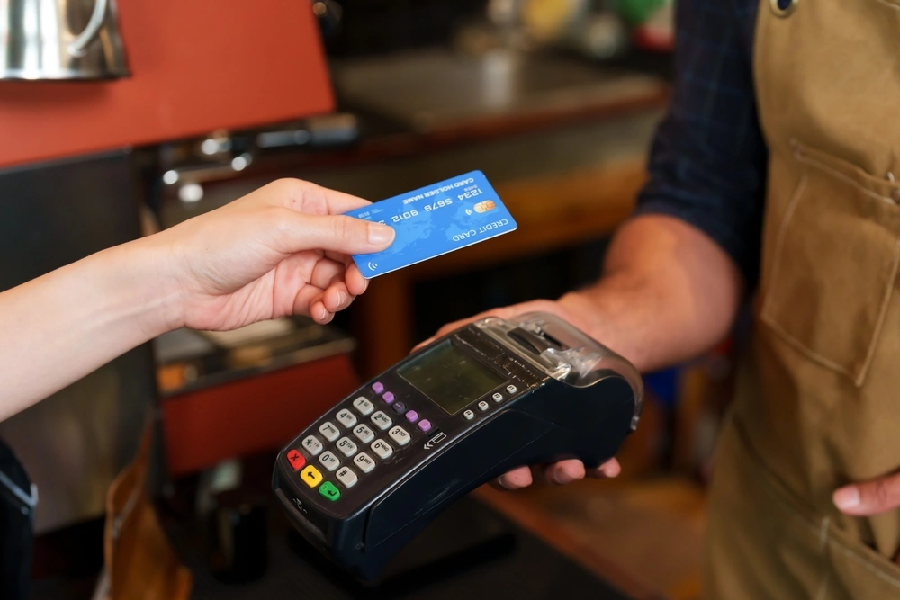 A close-up of a customer making a payment using a credit card on a point-of-sale (POS) terminal held by a cashier in a café